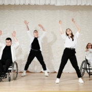 Four performers dance on a stage. Two are standing and two are in wheelchairs.